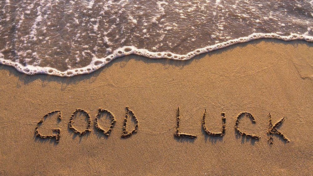 Good Luck written in the sand on the beach with sea foam approaching