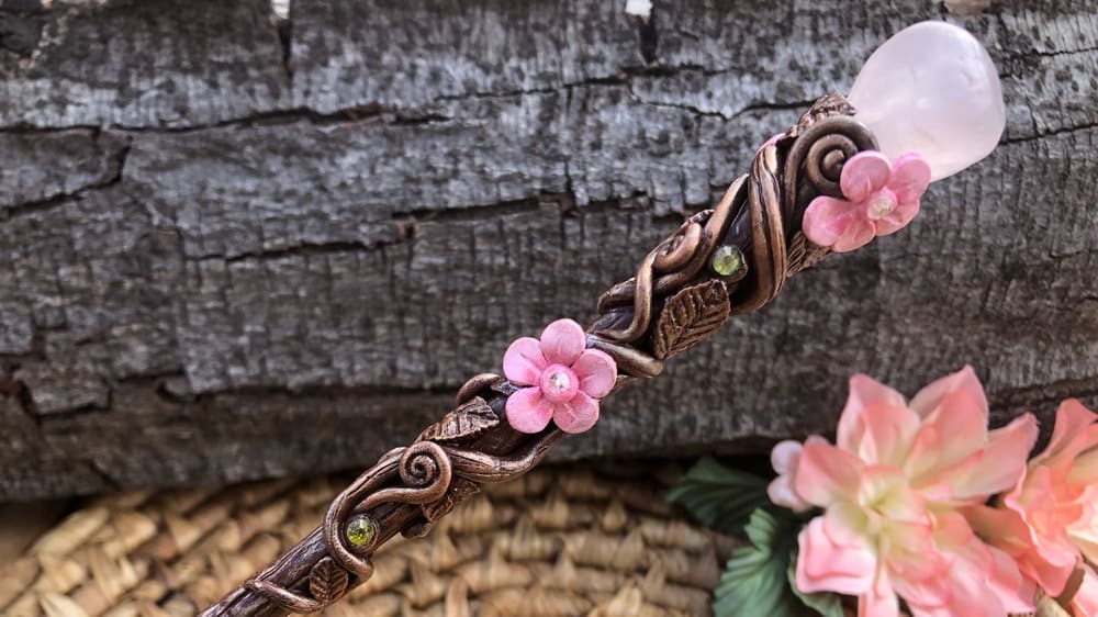A beautifully wand adorned with vines and flowers and a rose quartz crystal on the butt
