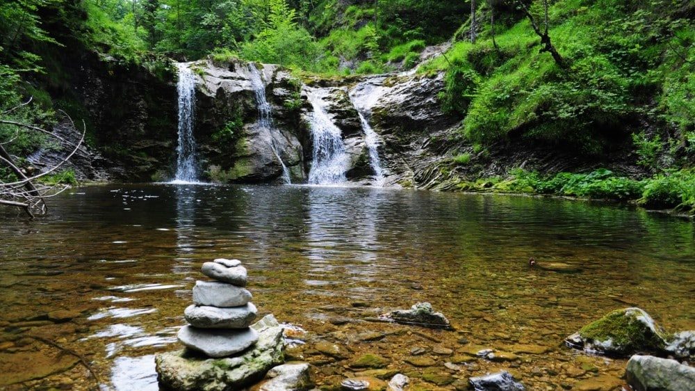a hidden pool in the forest fed by a waterfall