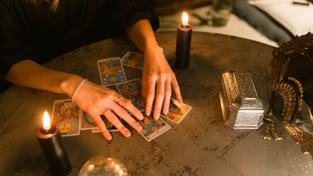 A bruja working with tarot cards on a table with black candles and a crystal ball