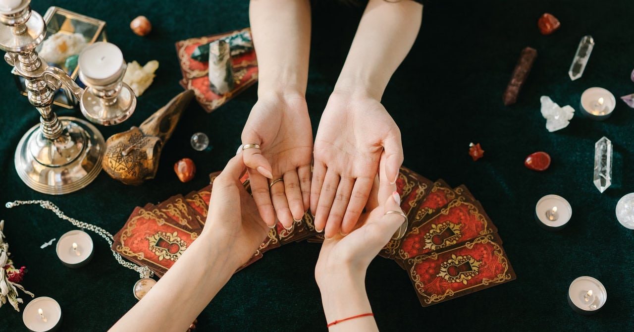 A woman reading another woman's palms with tarot cards, candles, crystals, and other magickal items around