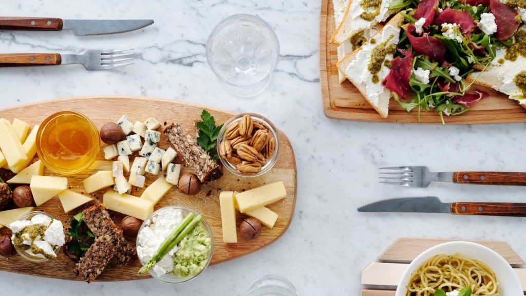 A spread with cheese, nuts, honey, greens, bread, meat, and grains