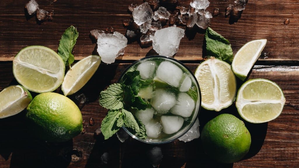 A mojito surrounded by ice, limes, and mint