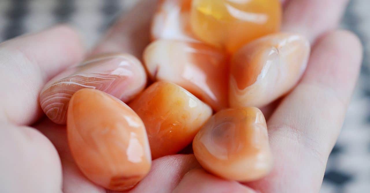 A hand holding Carnelian stones with smooth, glossy surfaces.