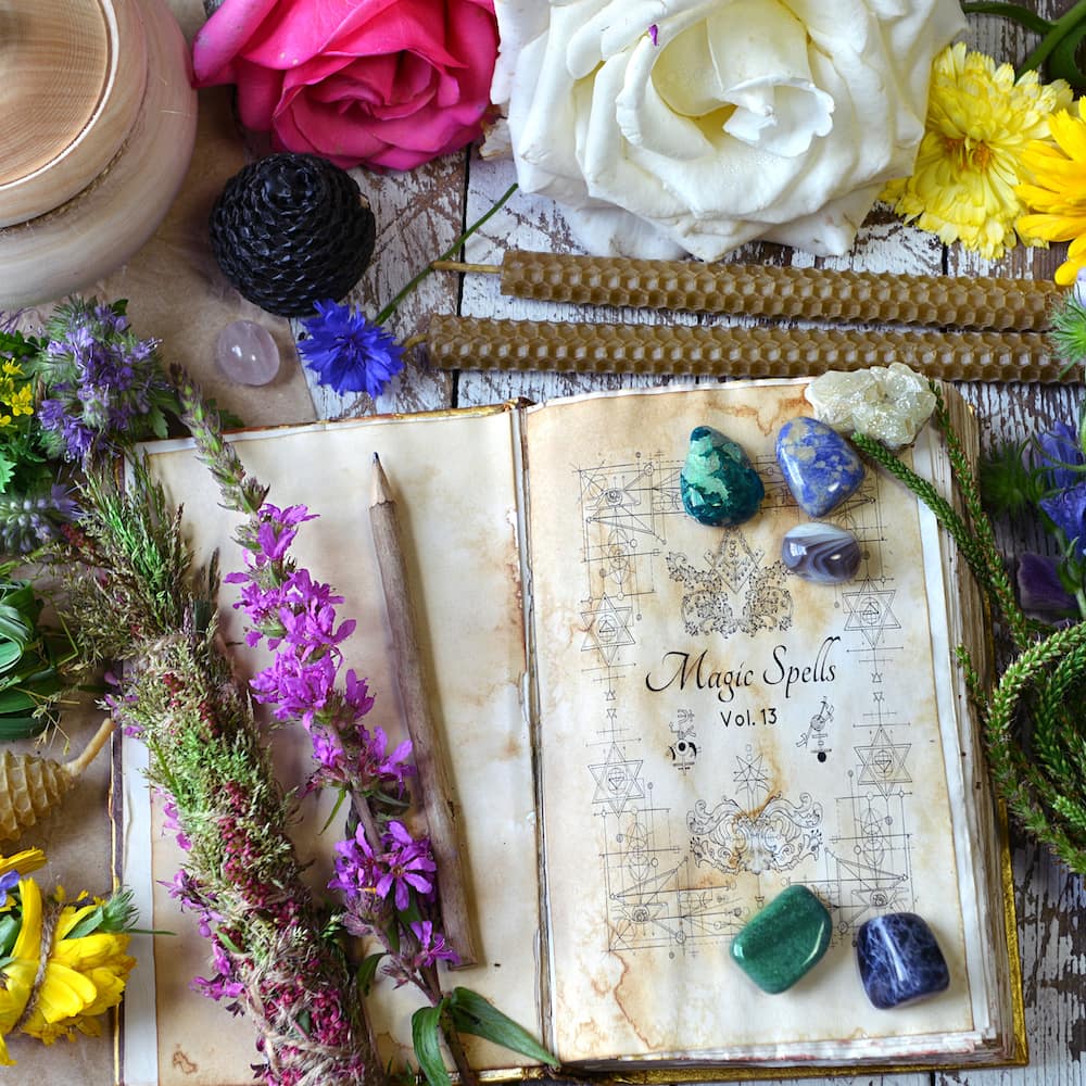 A book of shadows surrounded by a variety of flowers and crystals