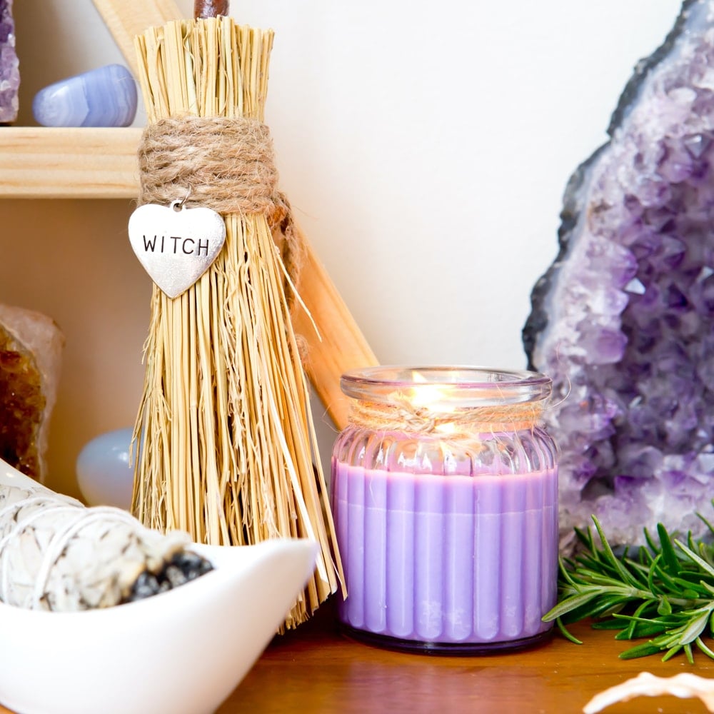 A wooden altar with a bundle of sage, a lavender candle, a broom, fresh rosemary, and a geode