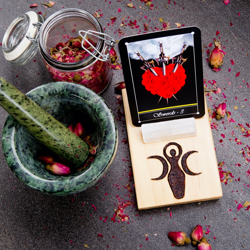 A tarot card on a wooden stand with a jar of rose buds and a mortar and pestle