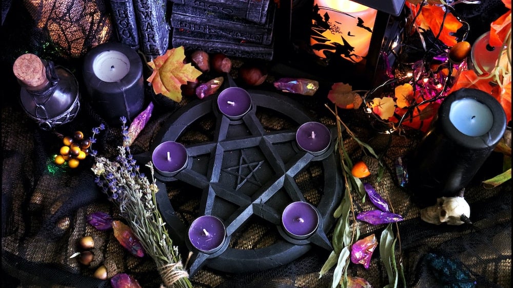 A Samhain altar featuring a sage, lavender, crystals, and pentagram candle holder with purple candles