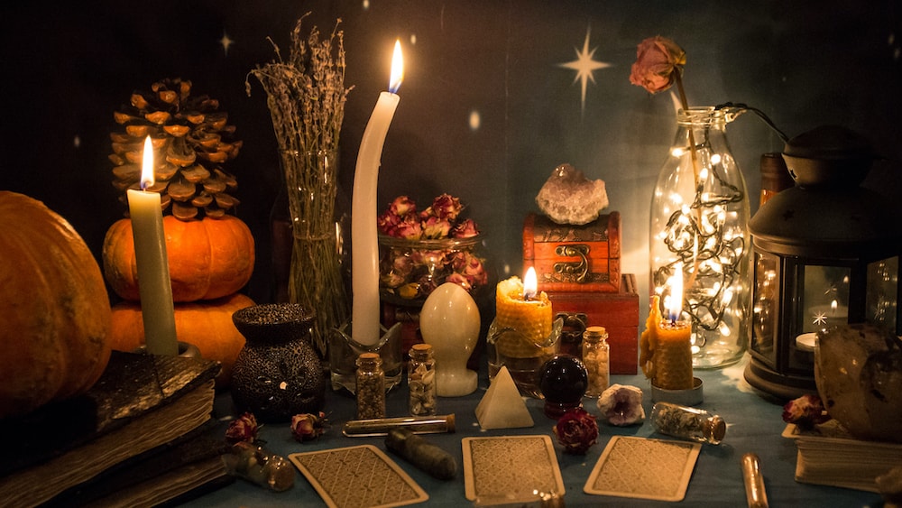 A Samhain altar with pumpkins, pinecones, roses, beeswax candles, crystals, tarot cards, and magickal ingredients