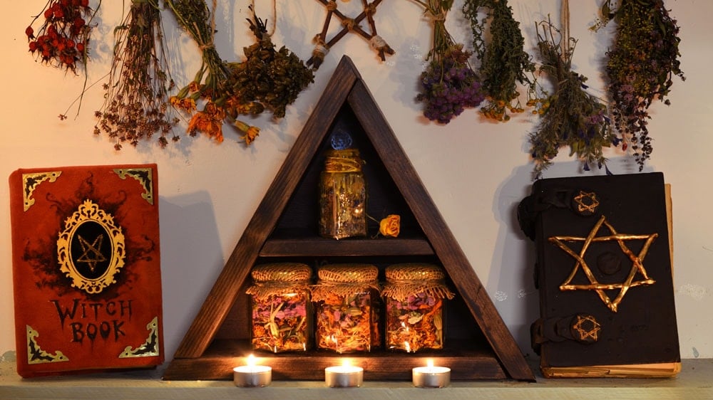 Witch bottles on an altar with lit candles in front and dried flowers and herbs behind