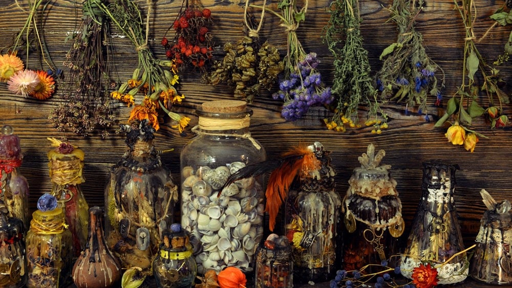 Many different spell bottles sealed with wax with dried herbs hanging above