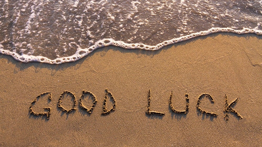 Good Luck written in the sand on the beach with sea foam approaching