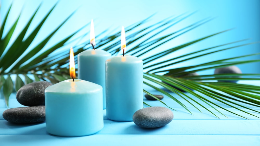 Light blue candles accompanied by smooth stones and a palm leaf with a matching light blue background