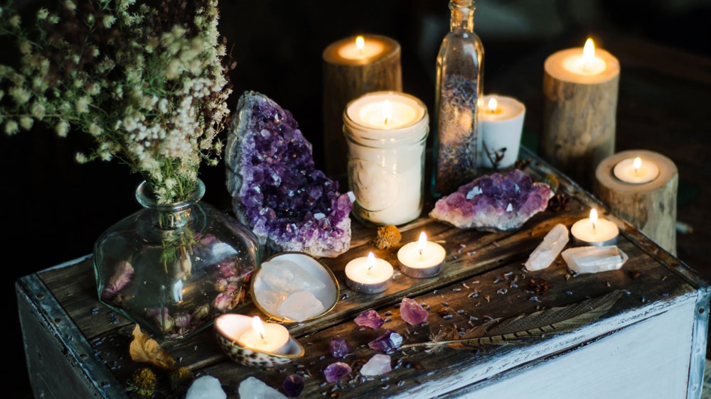 An altra featuring white candles, purple crystals, dried flowers, and a feather