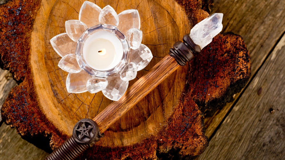 A wooden wand with a clear quartz tip laying on a wooden plate next to a white candle