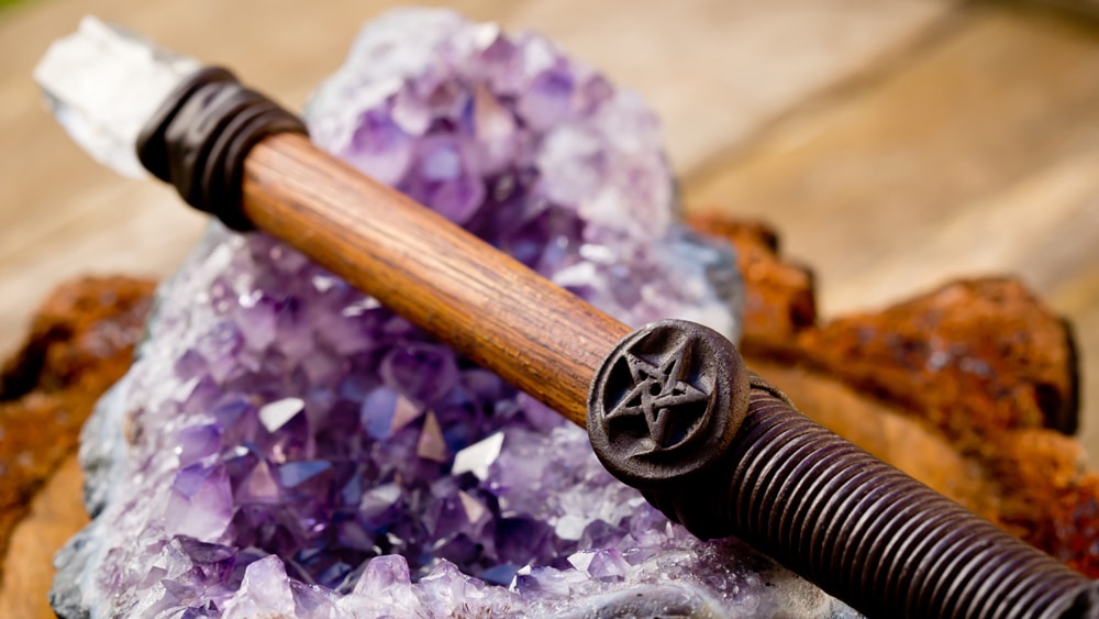 A wooden wand with a clear quartz tip laying on a purple geode crystal