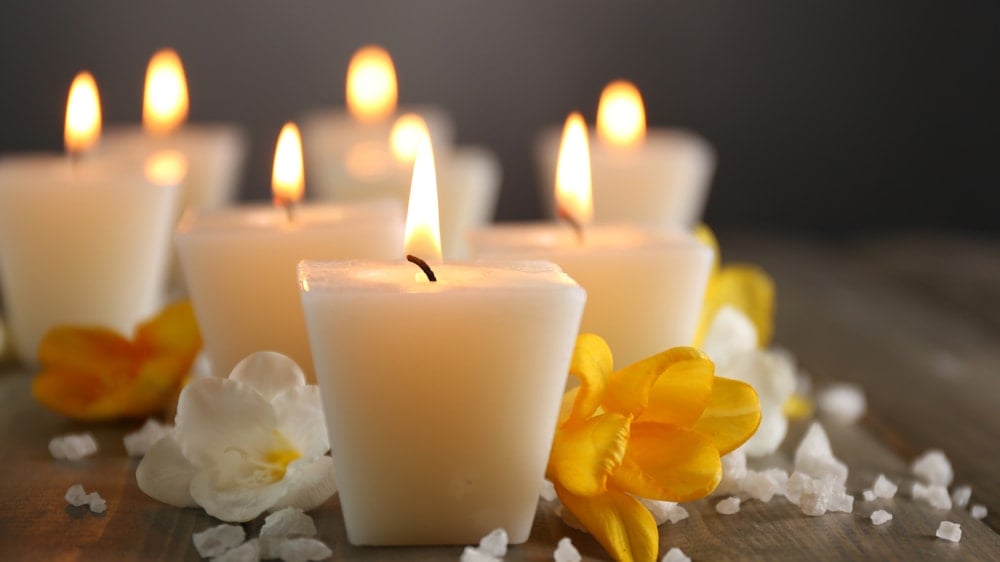 White candles on a wooden table with white and yellow flowers and salt