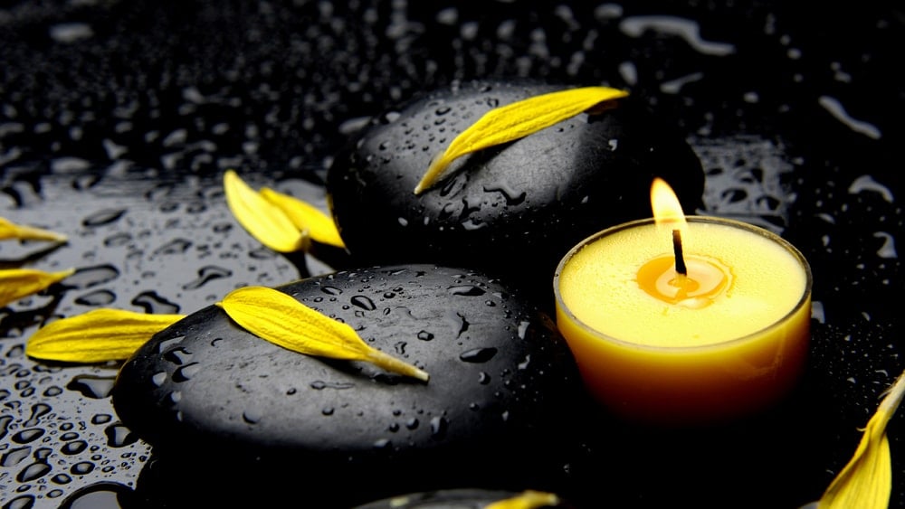 Vibrant yellow candle and flower petals on a wet black background with black stones