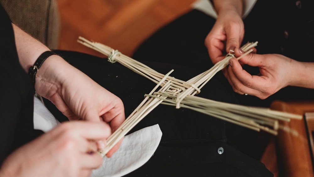 Two people weaving a Brigid cross