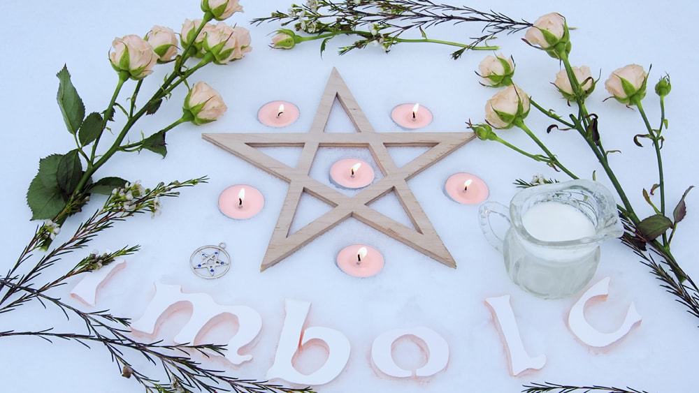 Imbolc Altar in the snow with flowers, candles, and sheep's milk