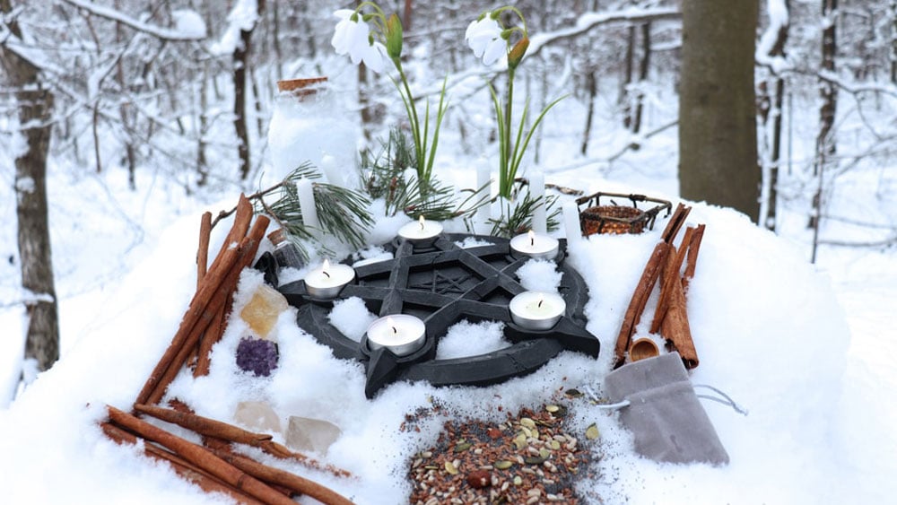 Imbolc Altar in the snow with nuts, seeds, crystals, snowdrop flowers, and cinnamon sticks