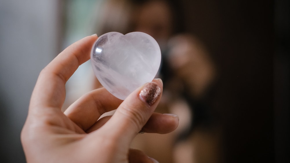 A hand holding a heart shaped rose quartz crystal