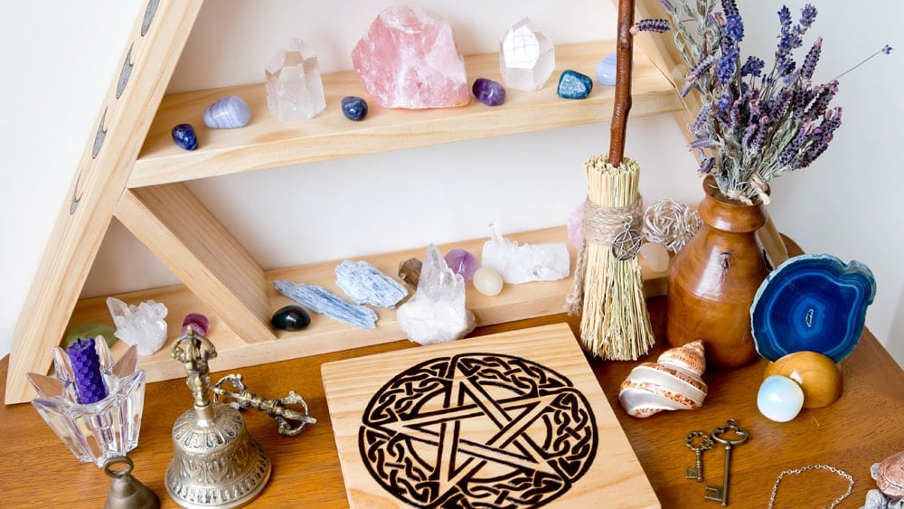 A beautiful Wiccan altar with a wood burned pentacle, various quartz crystals, a purple beeswax candle, bells, keys, a broom, and a bouquet of lavender