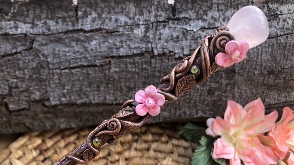 A beautifully wand adorned with vines and flowers and a rose quartz crystal on the butt