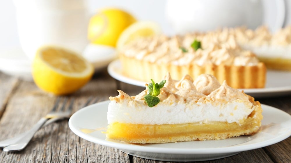 A lemon meringue pie with sliced lemons in the background