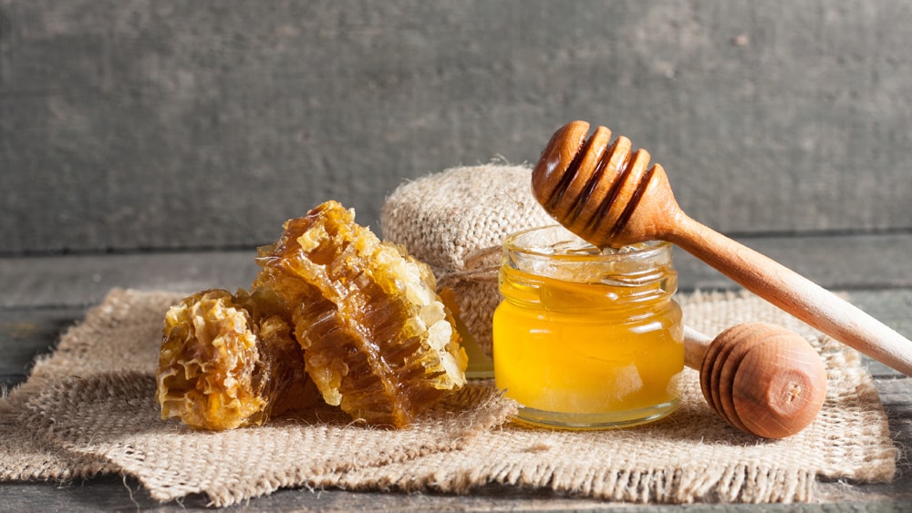 A jar of honey next to honeycomb