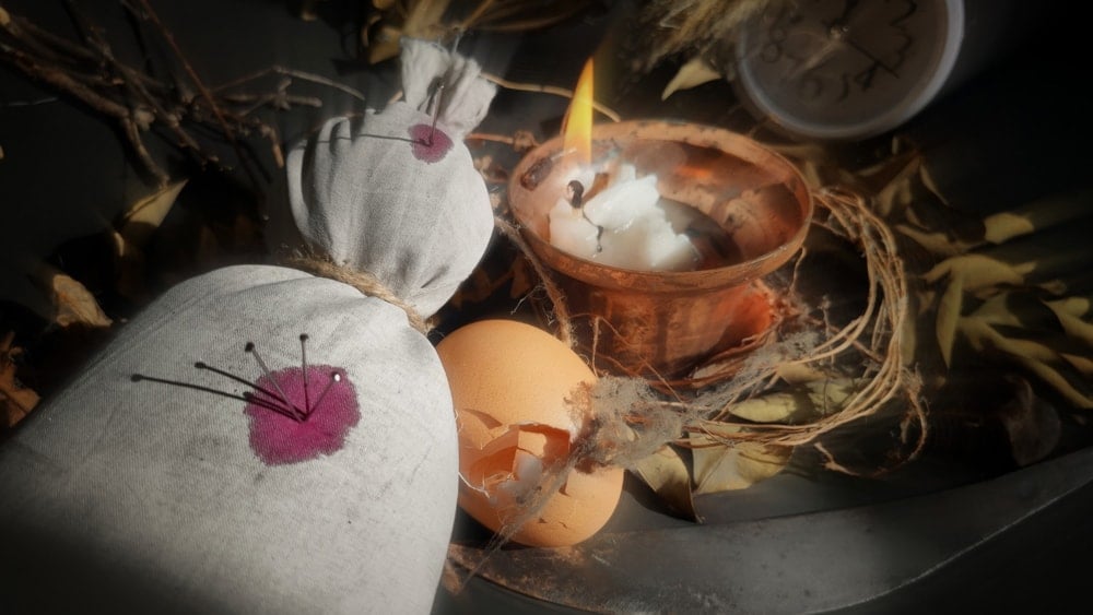 A Hoodoo doll next to a burning candle and an eggshell