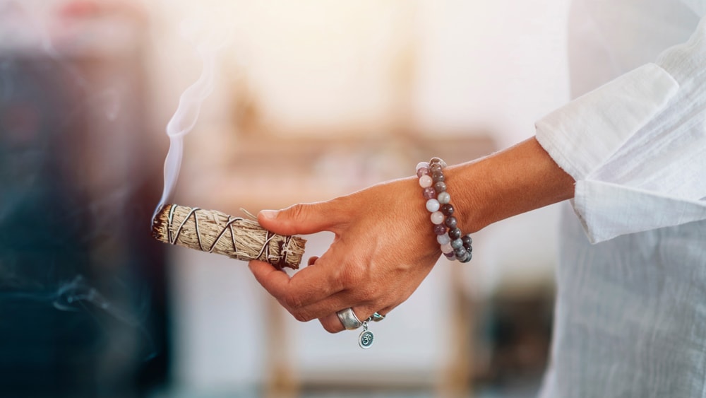 A woman smudging with a smoking bundle of dried sage