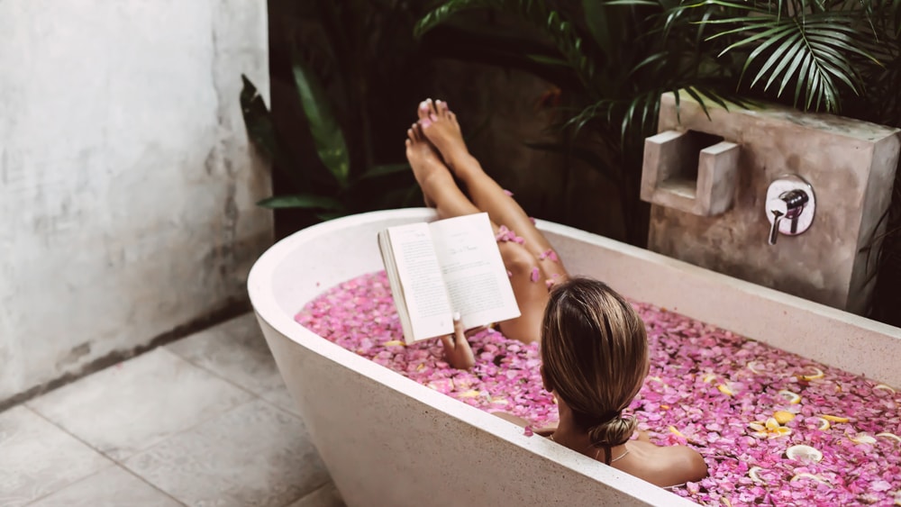 A woman reading a book in a bathtub filled with flower petals and citrus