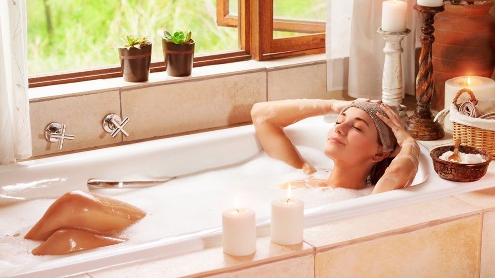 A woman relaxing in a bubble bath with candles lit