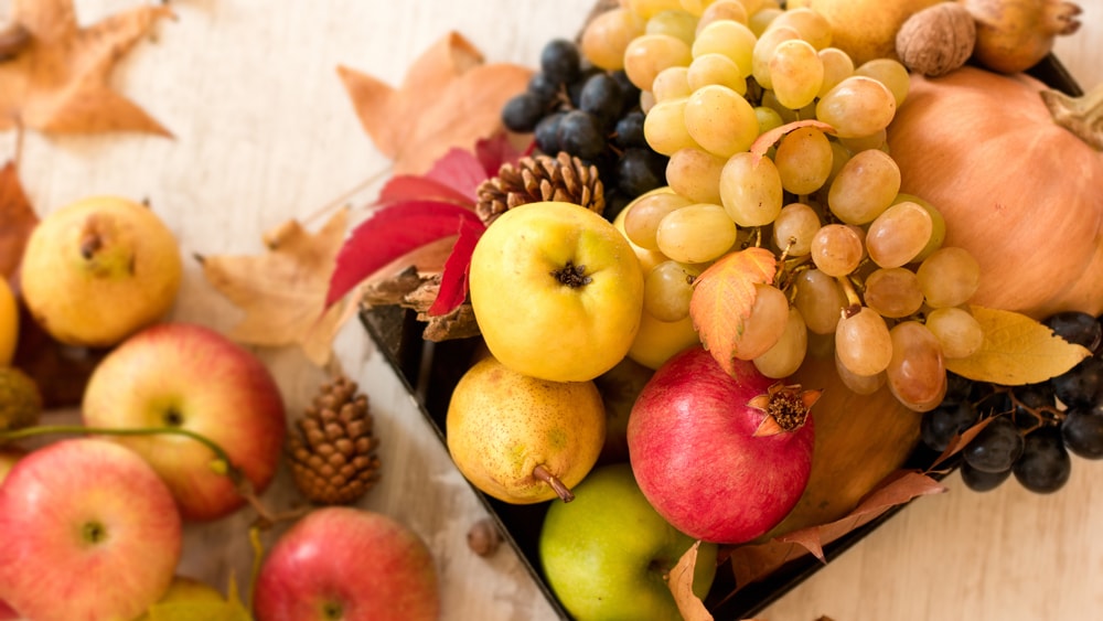 A basket filled with apples, grapes, pears, pomegranate, and pine cones