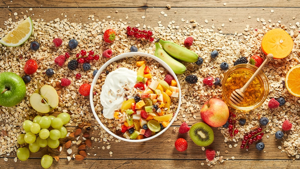 A table covered with oats, honey, nuts,  grapes, apples, berries, and citrus