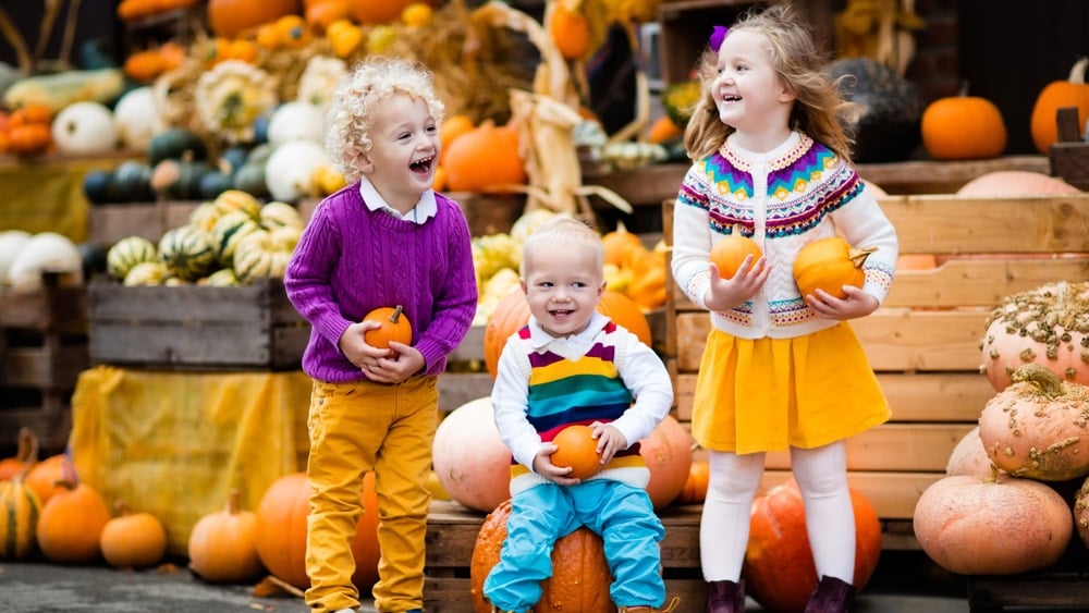 Three happy children holding pumpkins at a harvest festival