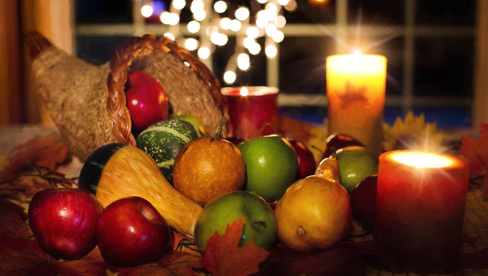 A cornucopia filled with harvest fruits and vegetables beside wine and a loaf of bread