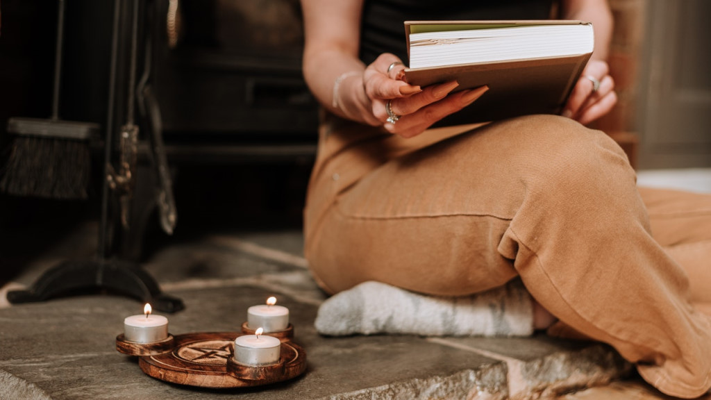 A witch holding a book beside a wooden pentacle candle holder