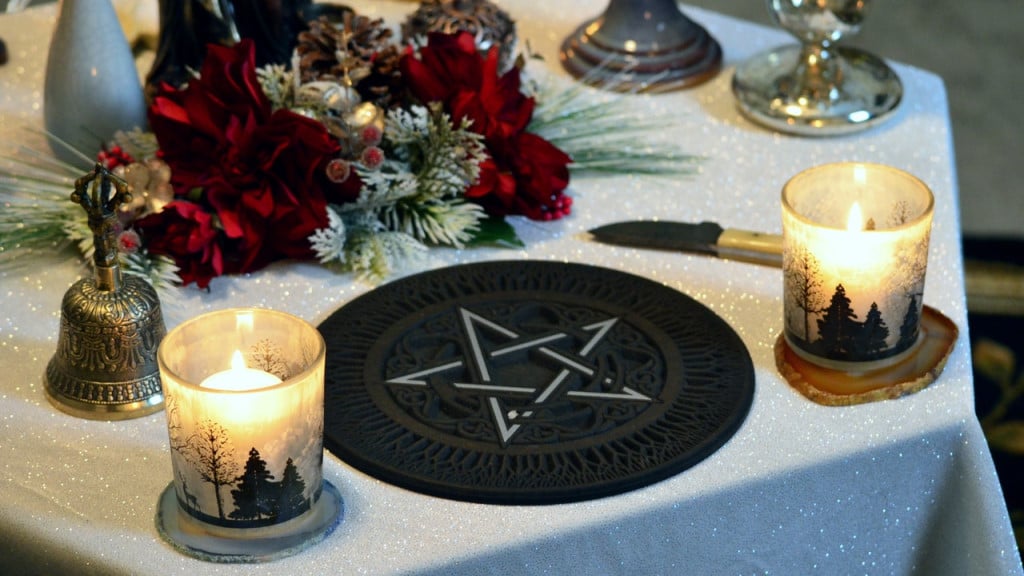 Yule altar with candles, a bell, a knife, red flowers, evergreen branches, and a black pentagram