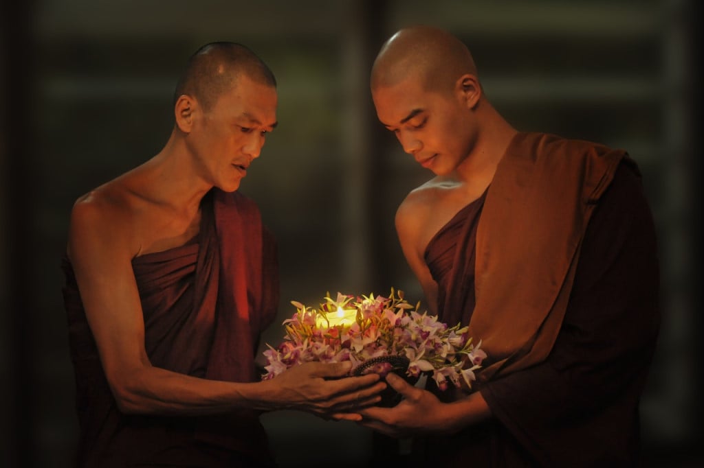 Buddhist monks holding a candle wrapped with flowers