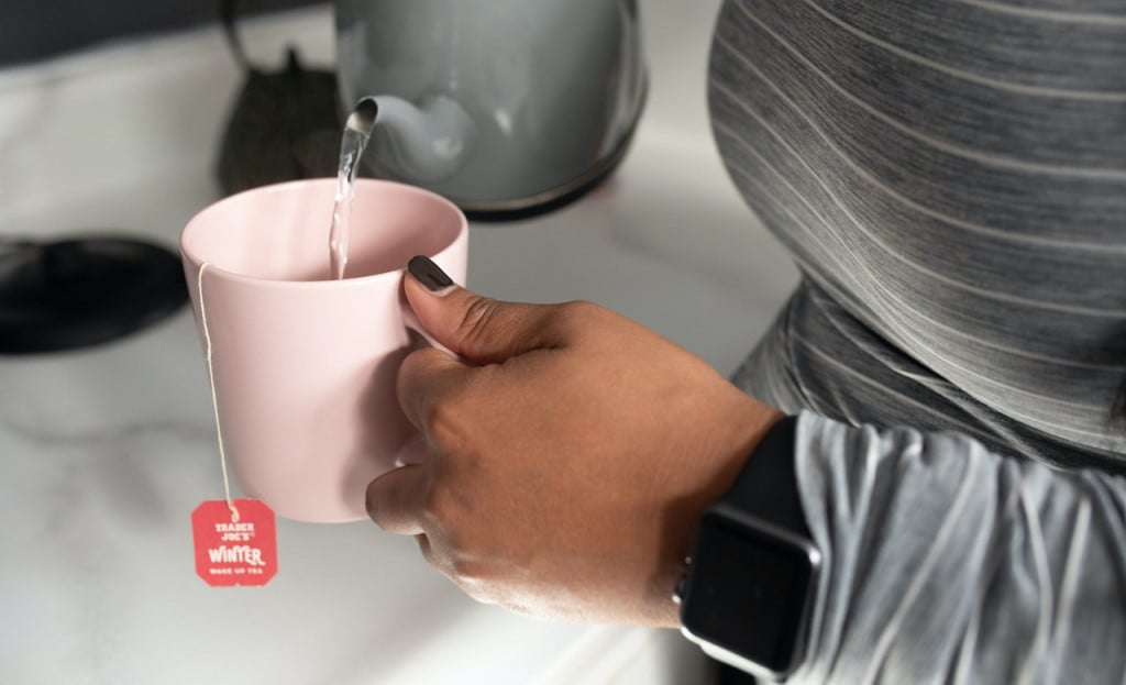 A woman pouring hot water into a mug with a teabag