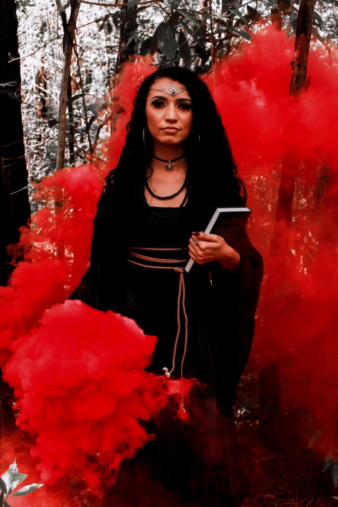 A pagan woman holding a book standing in a cloud of red smoke