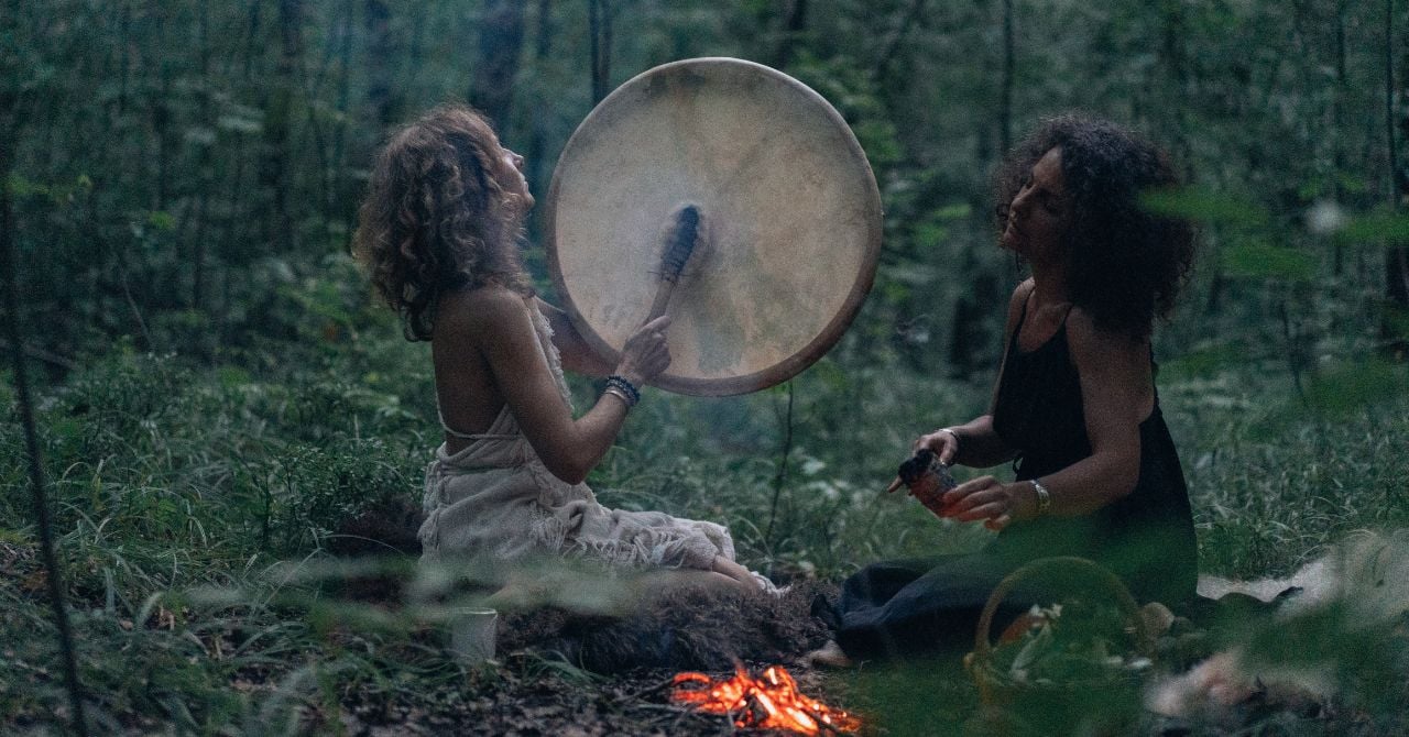 two witches in a forest beating a drum