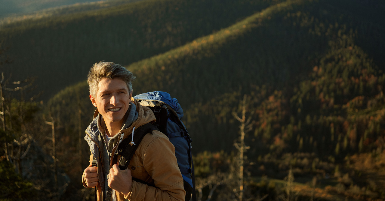 Hiker man with backpack enjoying nature and looking happy on top of mountain